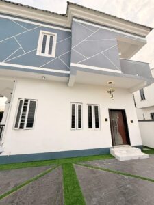 Front facade of a modern duplex featuring geometric exterior accents, balcony, and landscaped compound.