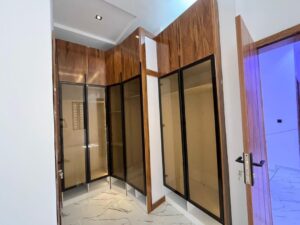 Modern walk-in closet with custom wooden wardrobes and glass-panel doors.